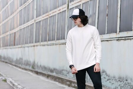 Man wearing white sweatshirt or hoodie, baseball cap and glasses outside on the city streets. Sweatshirt or hoodie for mock up, logo designs or design prints with free space.の写真素材