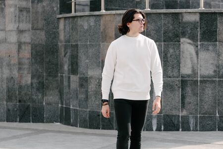 Man wearing white sweatshirt or hoodie and glasses outside on the city streets. Sweatshirt or hoodie for mock up, logo designs or design prints with free spaceの写真素材