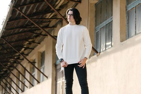 Man wearing white sweatshirt or hoodie and glasses outside on the city streets. Sweatshirt or hoodie for mock up, logo designs or design prints with free space.の写真素材