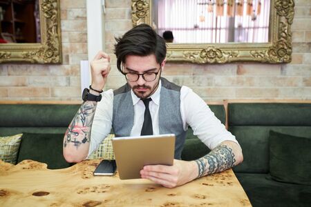 Handsome elegant businessman sitting at reastaurant and reading on tablet.の写真素材