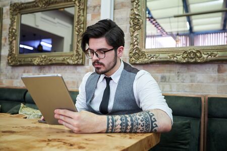 Handsome elegant businessman sitting at reastaurant and reading on tablet.の写真素材