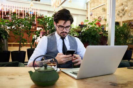 Young handsome man sitting in a restaurant and working on laptopの写真素材