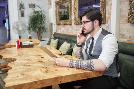 Handsome elegant businessman sitting at reastaurant and reading on tablet.の写真素材