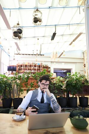 Young handsome man sitting in a restaurant and working on laptopの写真素材