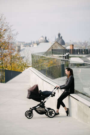 Mother with a pram or stroller on modern city streets walking and relaxing in autumn