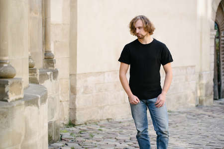 Hipster handsome male model wearing black blank t-shirt with space for your logo or design in casual urban style on europian streetsの写真素材
