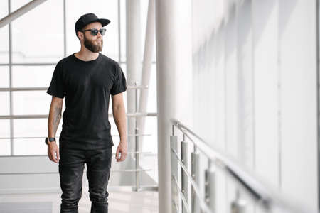 Hipster handsome male model with beard wearing black blank t-shirt and a baseball cap with space for your   design in casual urban styleの写真素材