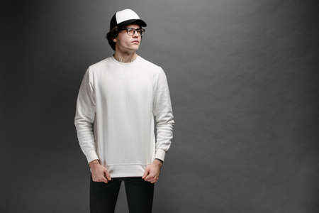 Man wearing blank white sweatshirt and empty baseball cap standing over gray background. Sweatshirt or hoodie for mock up,  designs or design print with with free space.の写真素材
