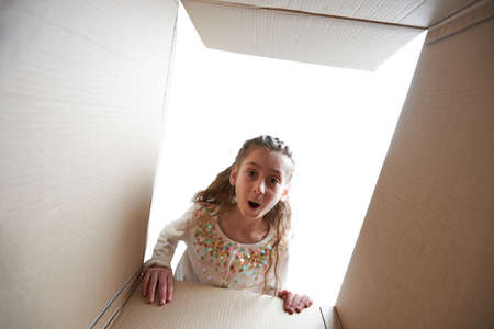 Child girl looking into a box with a present. She is happy and smilingの写真素材