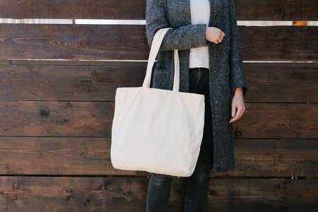 Woman holding white textile tote eco bag in urban area. Ecology or environment protection concept. White eco bag for mock up.の写真素材