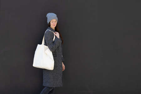 Woman holding white textile tote eco bag in urban area. Ecology or environment protection concept. White eco bag for mock up.の写真素材