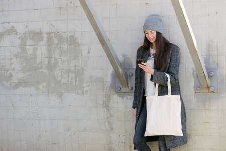 Woman holding white textile tote eco bag in urban area. Ecology or environment protection concept. White eco bag for mock up.の写真素材