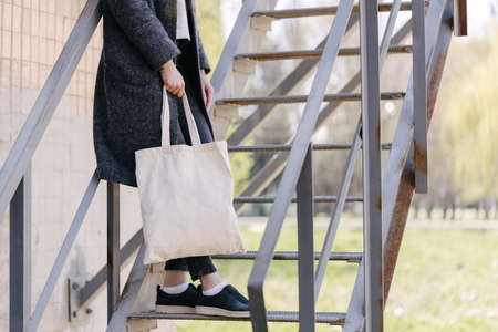 Woman holding white textile tote eco bag in urban area. Ecology or environment protection concept. White eco bag for mock up.の写真素材