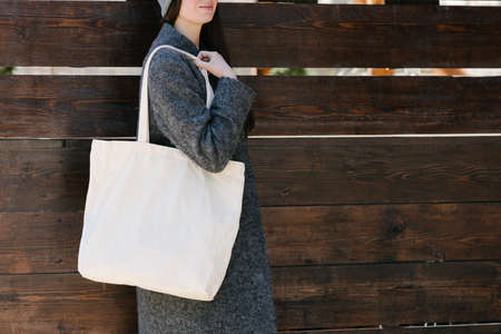 Woman holding white textile tote eco bag in urban area. Ecology or environment protection concept. White eco bag for mock up.の写真素材