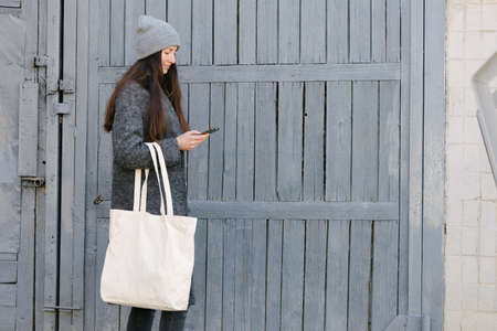 Woman holding white textile tote eco bag in urban area. Ecology or environment protection concept. White eco bag for mock up.の写真素材