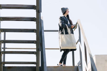 Woman holding white textile tote eco bag in urban area. Ecology or environment protection concept. White eco bag for mock up.の写真素材
