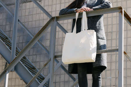 Woman holding white textile tote eco bag in urban area. Ecology or environment protection concept. White eco bag for mock up.の写真素材
