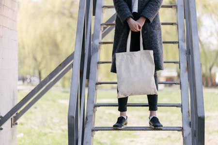 Woman holding white textile tote eco bag in urban area. Ecology or environment protection concept. White eco bag for mock up.の写真素材