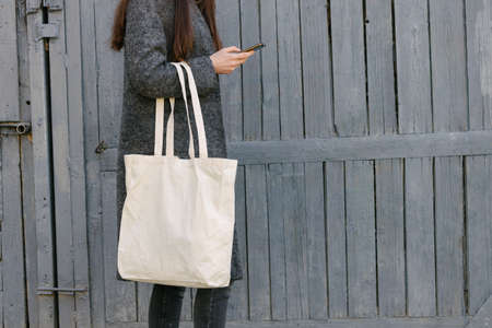 Woman holding white textile tote eco bag in urban area. Ecology or environment protection concept. White eco bag for mock up.の写真素材