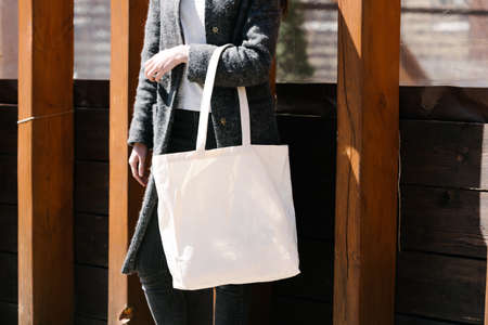 Woman holding white textile tote eco bag in urban area. Ecology or environment protection concept. White eco bag for mock up.の写真素材