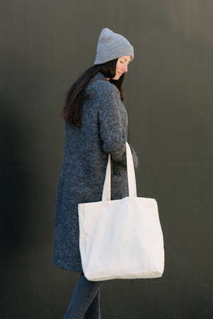 Woman holding white textile tote eco bag in urban area. Ecology or environment protection concept. White eco bag for mock up.の写真素材