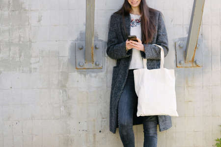 Woman holding white textile tote eco bag in urban area. Ecology or environment protection concept. White eco bag for mock up.の写真素材