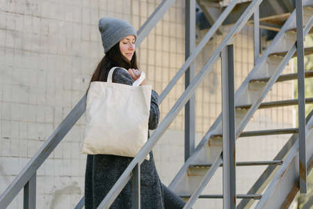 Woman holding white textile tote eco bag in urban area. Ecology or environment protection concept. White eco bag for mock up.の写真素材