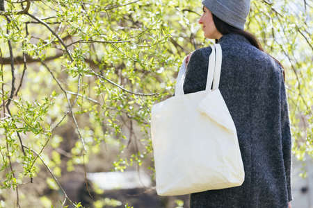 Woman holding white textile tote eco bag in urban area. Ecology or environment protection concept. White eco bag for mock up.の写真素材