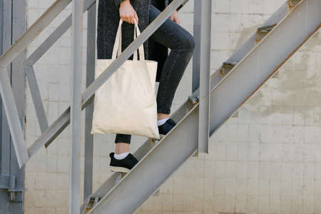 Woman holding white textile tote eco bag in urban area. Ecology or environment protection concept. White eco bag for mock up.の写真素材