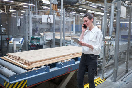 Business woman worker in the carpentry factory using tablet pc. Carpentry factory. Factory for the production of parquet boardの写真素材