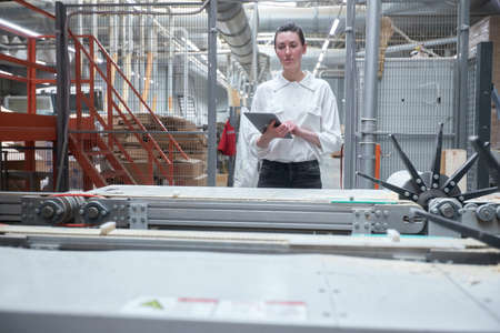 Business woman worker in the carpentry factory using tablet pc. Carpentry factory. Factory for the production of parquet boardの写真素材