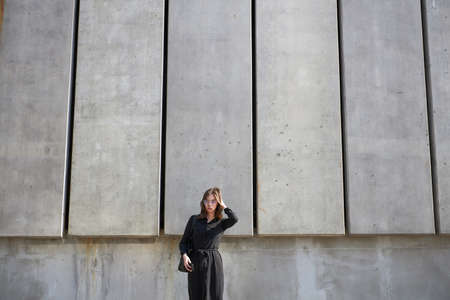 Business woman portrait in city streets at sunset. Sexy brunette wearing black dress, glasses and black leather bag outdoorの写真素材
