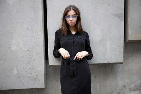 Fashion portrait of a sexy brunette woman with a make up wearing black clothes. She is wearing black modern dress, white sneakers and glassesの写真素材