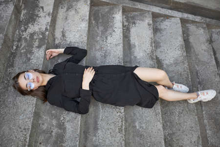 Sexy brunette woman with a make up wearing black modern trendy dress lying on cement stairwayの写真素材