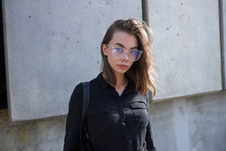Fashion portrait of a sexy brunette woman with a make up wearing black clothes. She is wearing black modern dress, white sneakers and glassesの写真素材