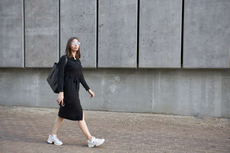 Fashion portrait of a sexy brunette woman with a make up wearing black clothes. She is wearing black modern dress, white sneakers and glassesの写真素材