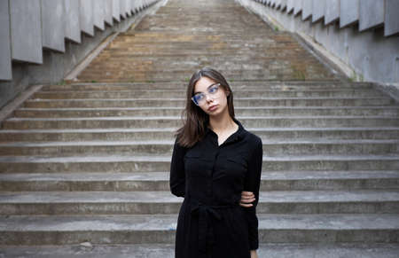 Fashion portrait of a sexy brunette woman with a make up wearing black clothes. She is wearing black modern dress, white sneakers and glassesの写真素材