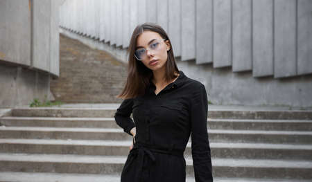 Fashion portrait of a sexy brunette woman with a make up wearing black clothes. She is wearing black modern dress, white sneakers and glassesの写真素材