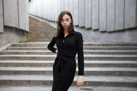 Fashion portrait of a sexy brunette woman with a make up wearing black clothes. She is wearing black modern dress, white sneakers and glassesの写真素材