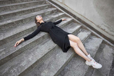 Sexy brunette woman with a make up wearing black modern trendy dress lying on cement stairwayの写真素材