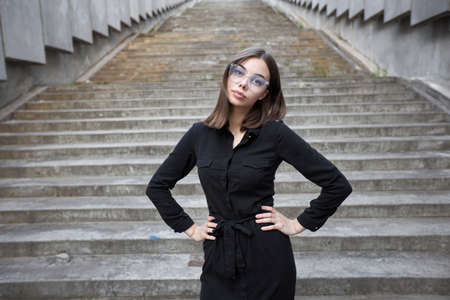 Fashion portrait of a sexy brunette woman with a make up wearing black clothes. She is wearing black modern dress, white sneakers and glassesの写真素材