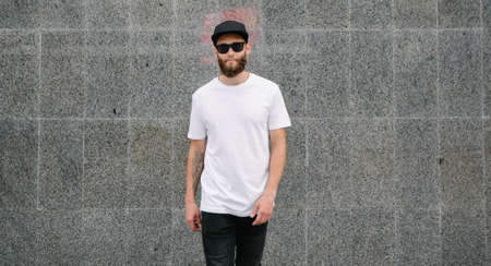 Hipster handsome male model with beard wearing white blank t-shirt and a baseball cap with space for your logo or design in casual urban styleの写真素材