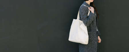 Woman holding white textile tote eco bag in urban area. Ecology or environment protection concept. White eco bag for mock up.の写真素材