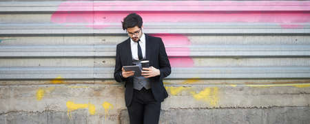 Businessman using a tablet pc outside on the city street wearing elegant clothesの写真素材