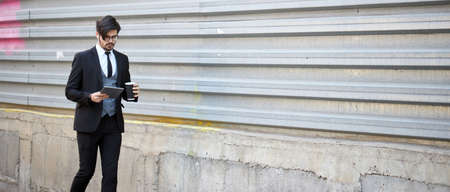 Businessman using a tablet pc outside on the city street wearing elegant clothesの写真素材