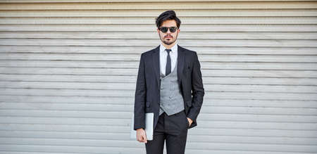 Businessman holding a laptop pc outside on the city street wearing elegant clothesの写真素材