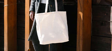Woman holding white textile tote eco bag in urban area. Ecology or environment protection concept. White eco bag for mock up.の写真素材