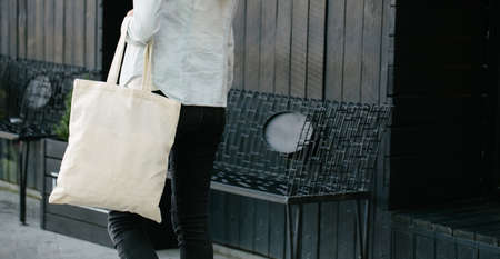 Woman holding white textile eco bag against urban city background. . Ecology or environment protection concept. White eco bag for mock up.の写真素材