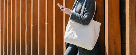 Woman holding white textile tote eco bag in urban area. Ecology or environment protection concept. White eco bag for mock up.の写真素材