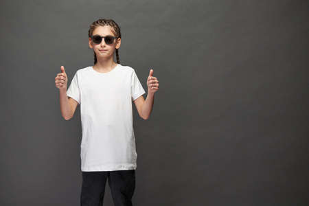 Kid girl wearing white t-shirt with space for your logo or design in studio over gray background with sunglassesの写真素材